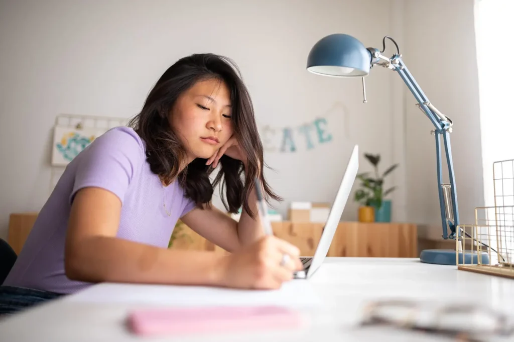 Generation Z วัยรุ่นผู้หญิงนั่งเขียนการบ้าน และใช้โน๊ตบุ๊คด้วย