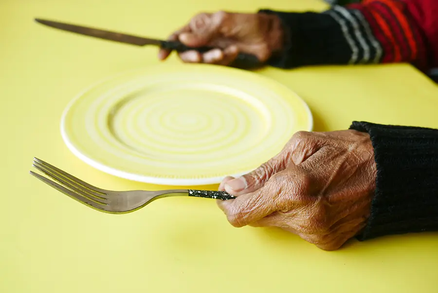 มือผู้สูงอายุจับช้อนส้อมมีจานวางอยู่บนโต๊ะ แต่ไม่มีอาหาร ภาวะทุพโภชนาการ ในผู้ป่วยหลอดเลือดสมอง 